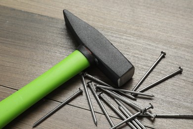 Photo of New hammer and metal nails on wooden table, closeup. Professional construction tool