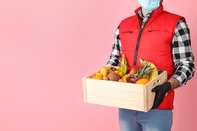 Courier holding crate with assortment of exotic fruits on pink background, closeup. Space for text