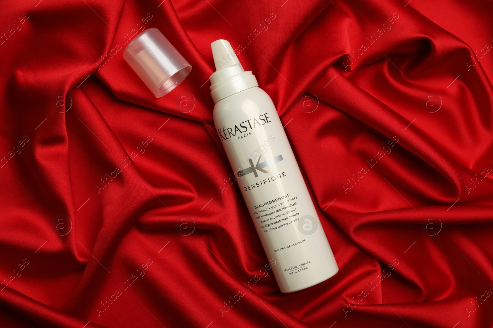 Photo of MYKOLAIV, UKRAINE - SEPTEMBER 08, 2021: Bottle of Kerastase hair care cosmetic product on red fabric, flat lay