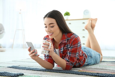 Photo of Attractive young woman using mobile phone while drinking coffee at home