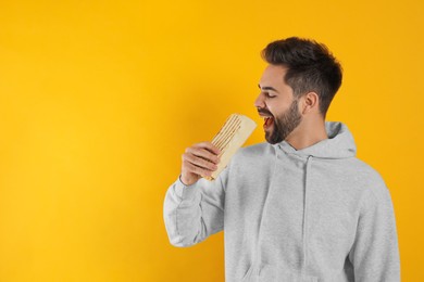 Young man eating tasty shawarma on yellow background. Space for text