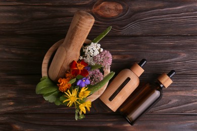Glass bottles of aromatic essential oil and mortar with different herbs on wooden table, flat lay
