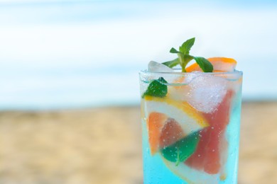 Photo of Glass of refreshing drink with grapefruit and mint near sea, closeup. Space for text