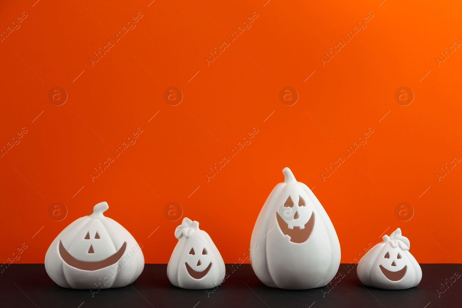 Photo of White pumpkin shaped candle holders on black table against orange background, space for text. Halloween decoration