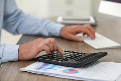 Professional accountant using calculator at wooden desk, closeup