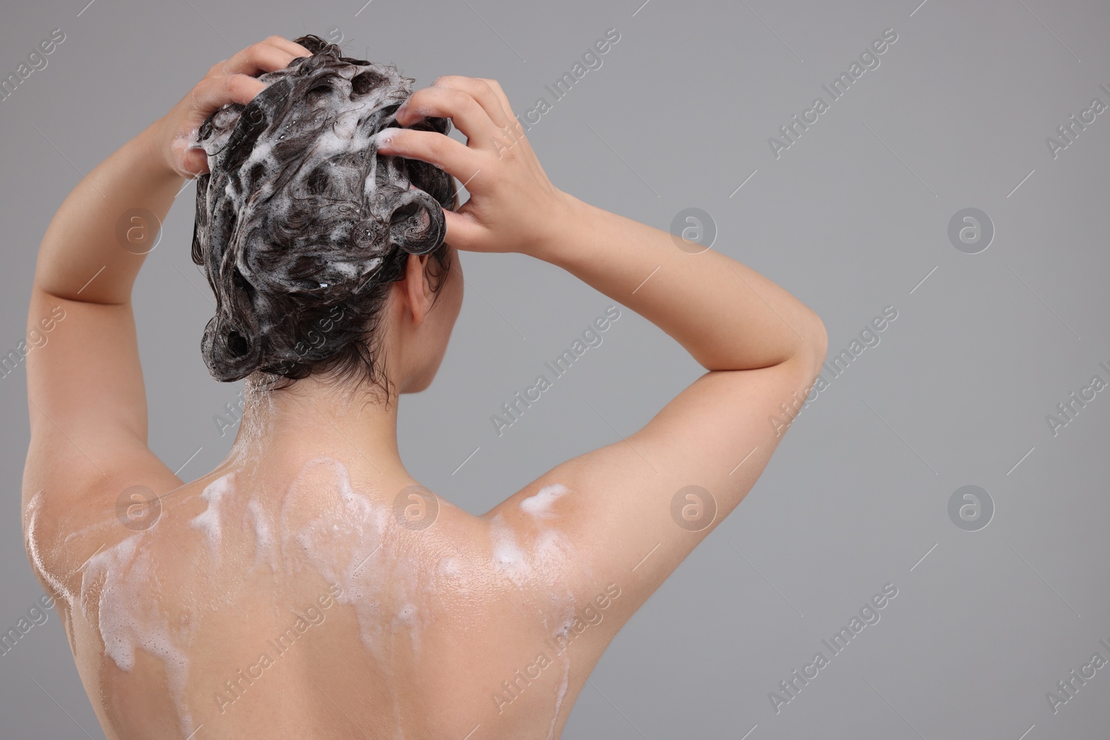 Photo of Woman washing hair on grey background, back view. Space for text