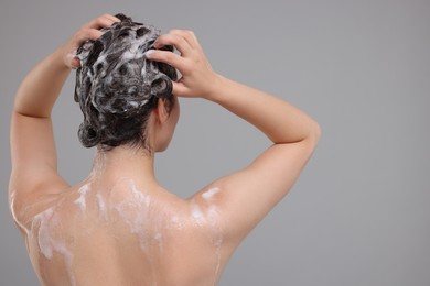 Woman washing hair on grey background, back view. Space for text