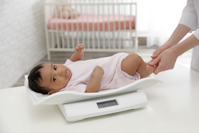 Photo of Doctor weighting African-American baby on scales in light room