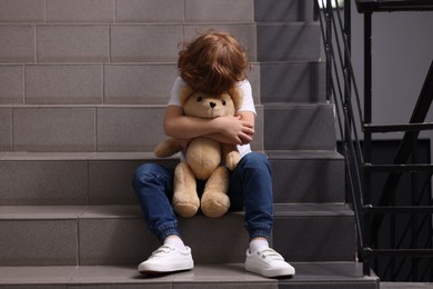 Photo of Child abuse. Upset boy with toy sitting on stairs