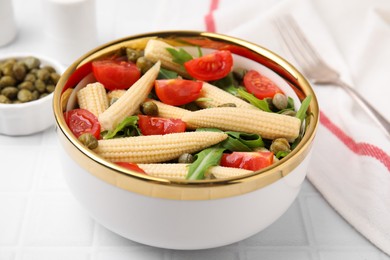 Photo of Tasty baby corn with tomatoes, arugula and capers on white tiled table, closeup