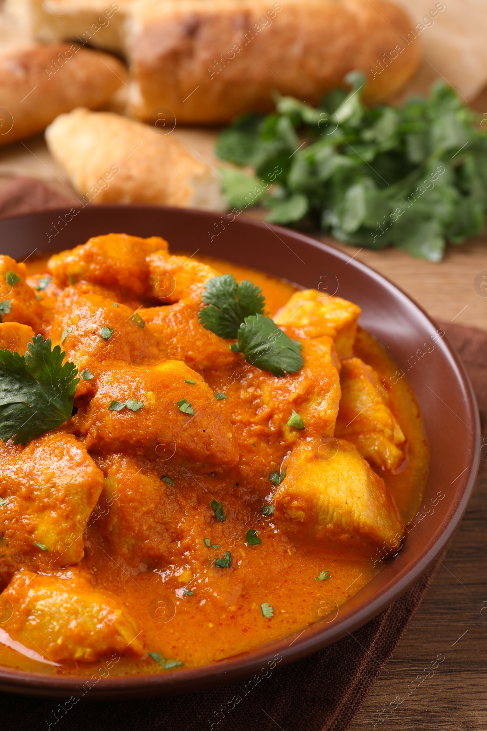 Photo of Bowl of delicious chicken curry on wooden table, closeup