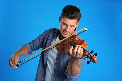 Happy man playing violin on light blue background