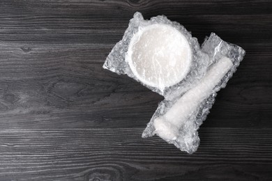 Mortar and pestle packed in bubble wrap on dark wooden table, flat lay. Space for text