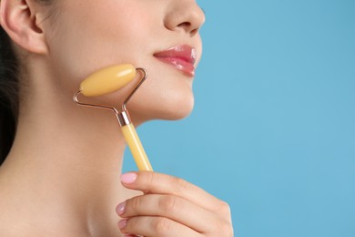 Woman using natural jade face roller on light blue background, closeup. Space for text