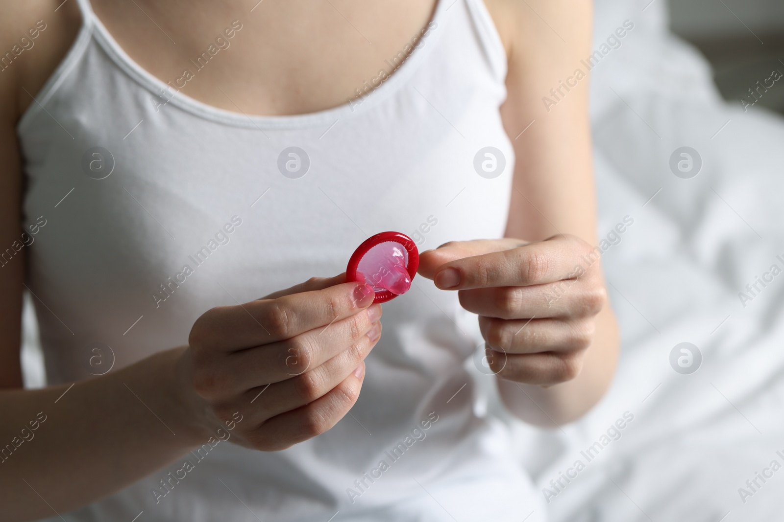 Photo of Woman holding unpacked condom on light background, closeup. Safe sex