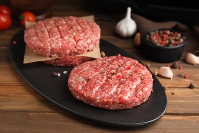 Photo of Raw hamburger patties with spices on wooden table