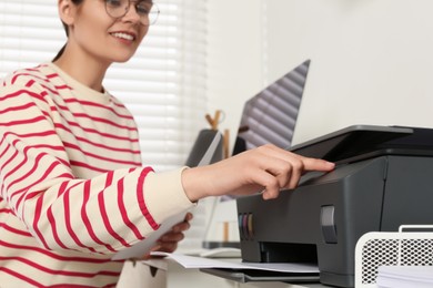 Photo of Woman using modern printer at workplace indoors, selective focus