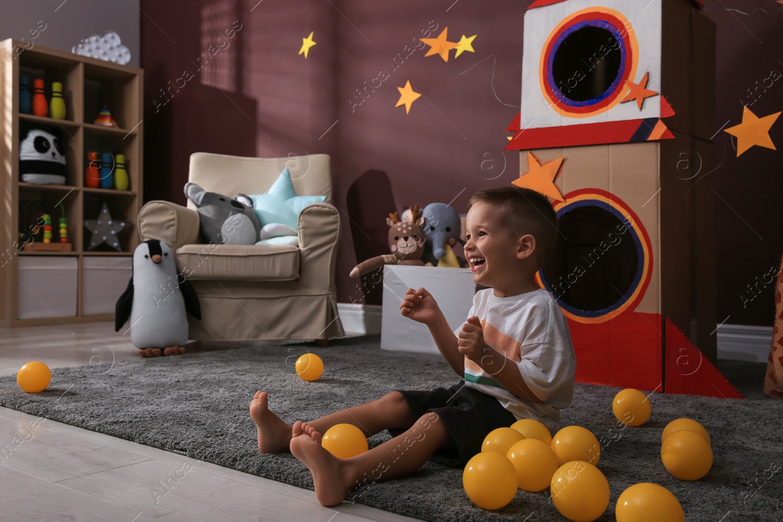 Photo of Cute little boy playing on floor near cardboard rocket  at home. Child's room interior