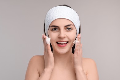 Young woman with headband washing her face on light grey background