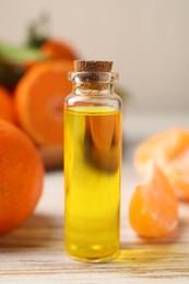 Bottle of tangerine essential oil and fresh fruits on white wooden table, closeup