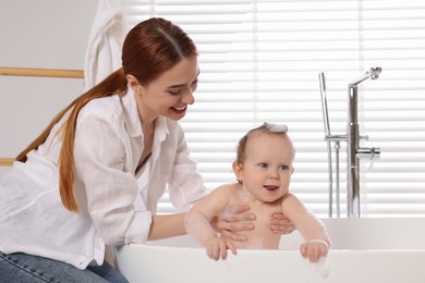 Mother washing her little baby in tub at home