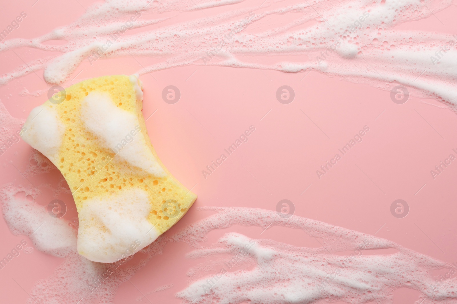 Photo of Yellow sponge with foam on pink background, top view. Space for text