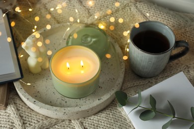 Photo of Tray with beautiful candles, eucalyptus, cup of tea and fairy lights on knitted blanket