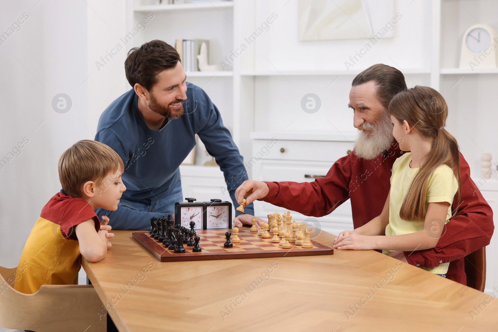 Photo of Family playing chess together at table in room