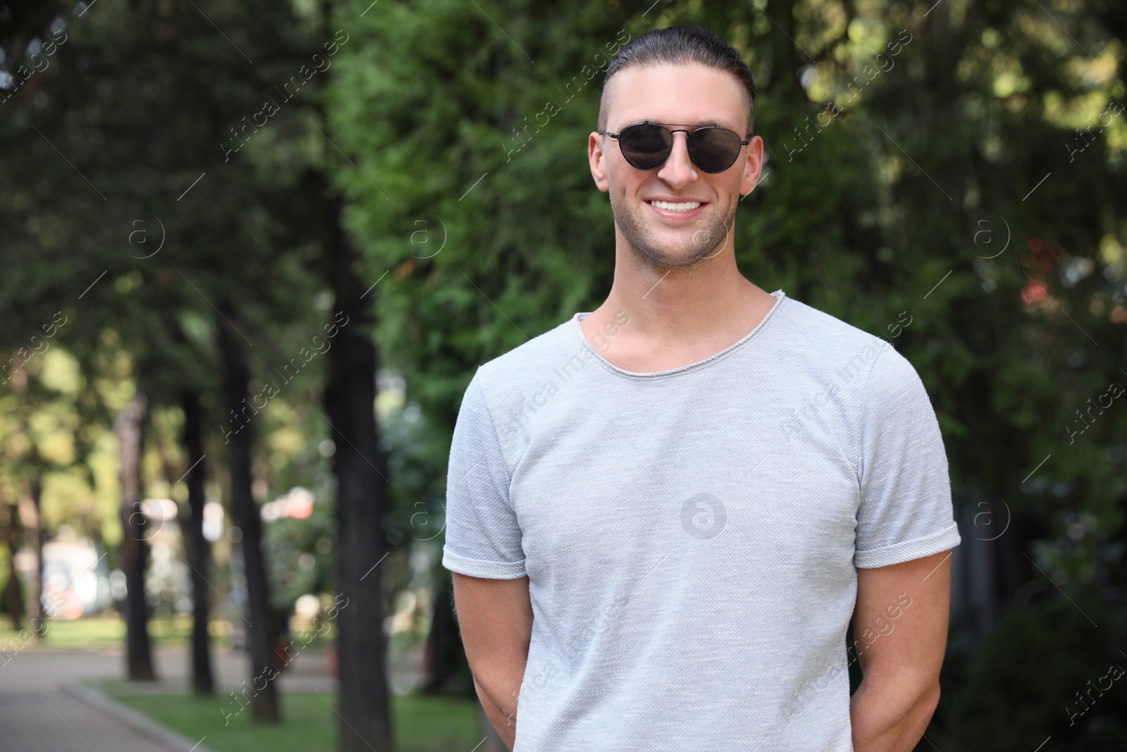 Photo of Handsome young man in stylish sunglasses at park, space for text