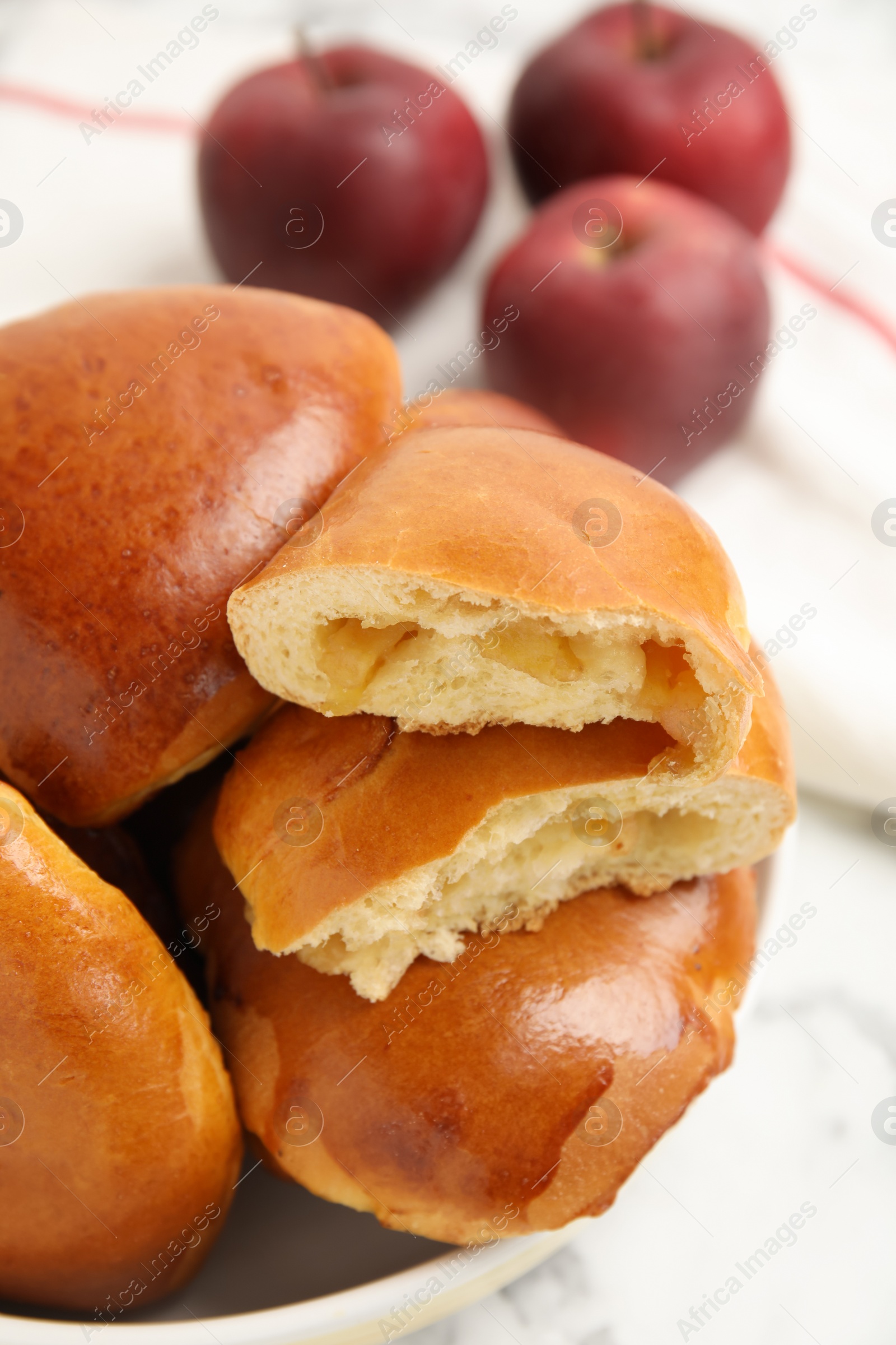 Photo of Delicious baked apple pirozhki in bowl on white marble table, closeup