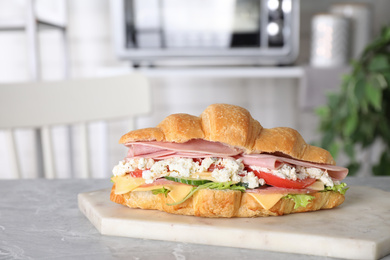 Photo of Tasty croissant sandwich with ham on grey marble table indoors