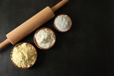 Photo of Rolling pin and different types of flour on black table, flat lay. Space for text