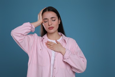 Photo of Young woman suffering from headache on blue background. Cold symptoms