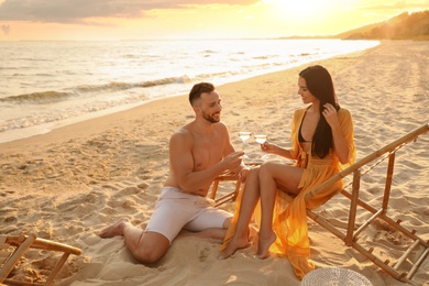 Photo of Romantic couple drinking wine together on beach at sunset