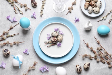 Festive Easter table setting with painted eggs and floral decor on light grey background, flat lay