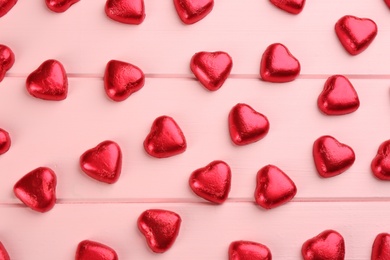 Heart shaped chocolate candies on pink wooden table, flat lay