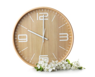 Photo of Big clock and branch with spring blossoms on table against white background. Time change concept