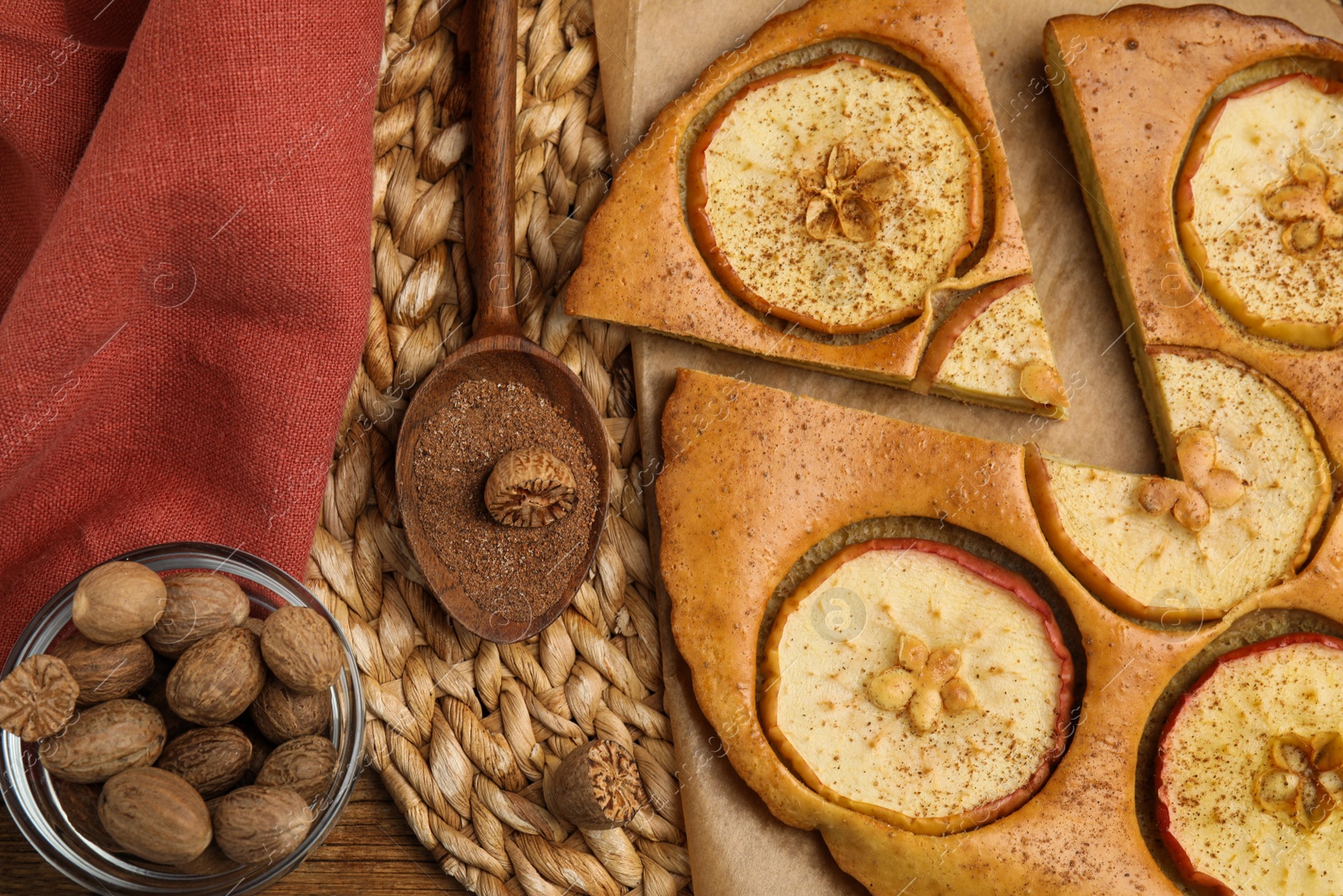 Photo of Tasty apple pie, nutmeg powder and seeds on wicker mat, flat lay