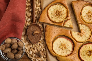 Tasty apple pie, nutmeg powder and seeds on wicker mat, flat lay