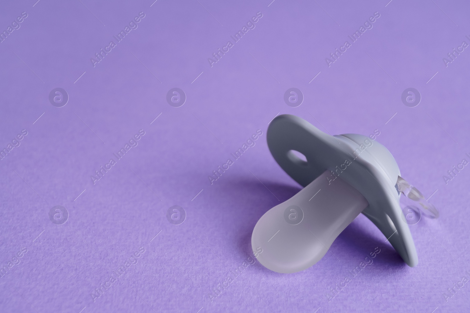 Photo of New baby pacifier on purple background, closeup. Space for text
