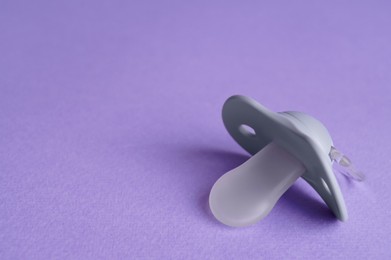 Photo of New baby pacifier on purple background, closeup. Space for text