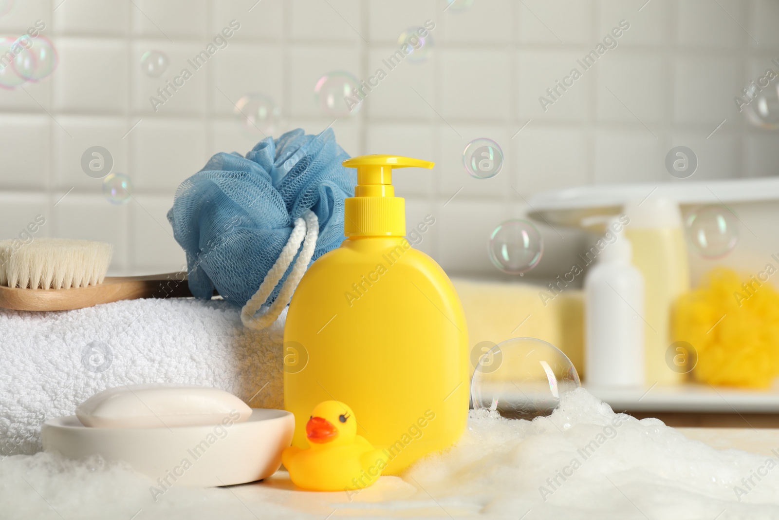 Photo of Baby cosmetic products, bath duck, brush and towel on white table against soap bubbles