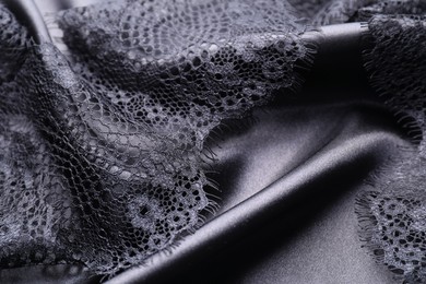 Photo of Beautiful lace with pattern on black fabric, closeup