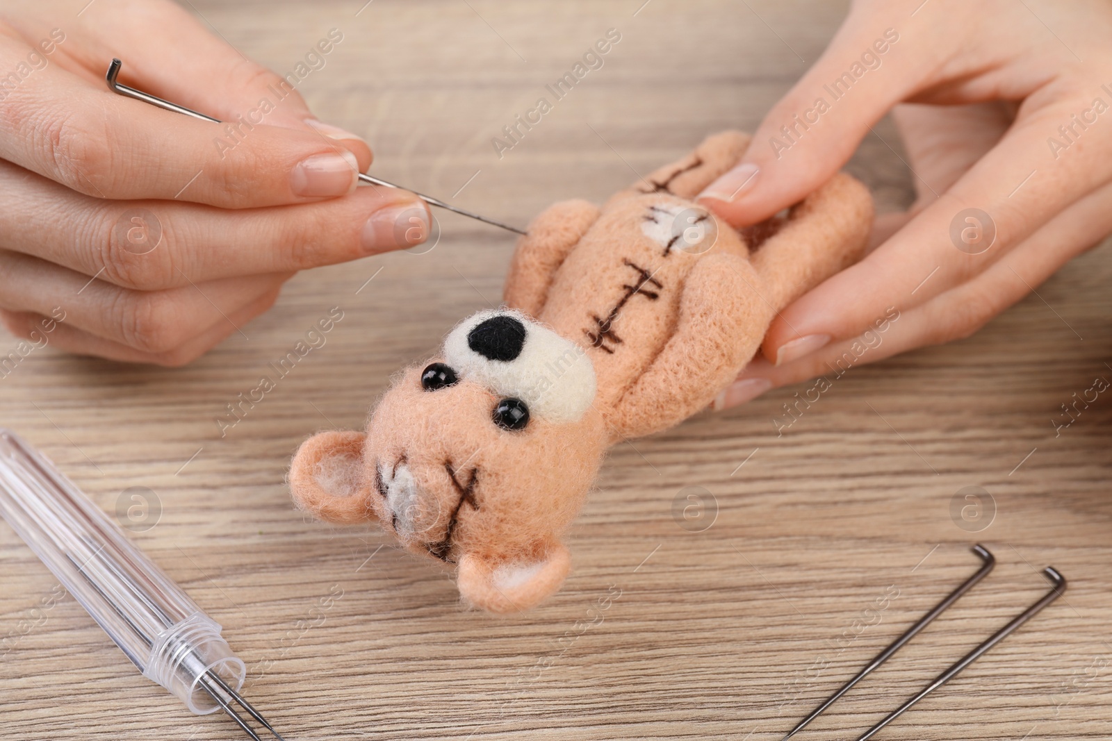 Photo of Woman felting cute toy bear from wool at wooden table, closeup