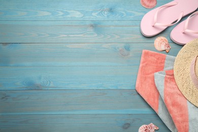 Beach towel, straw hat and flip flops on light blue wooden background, flat lay. Space for text