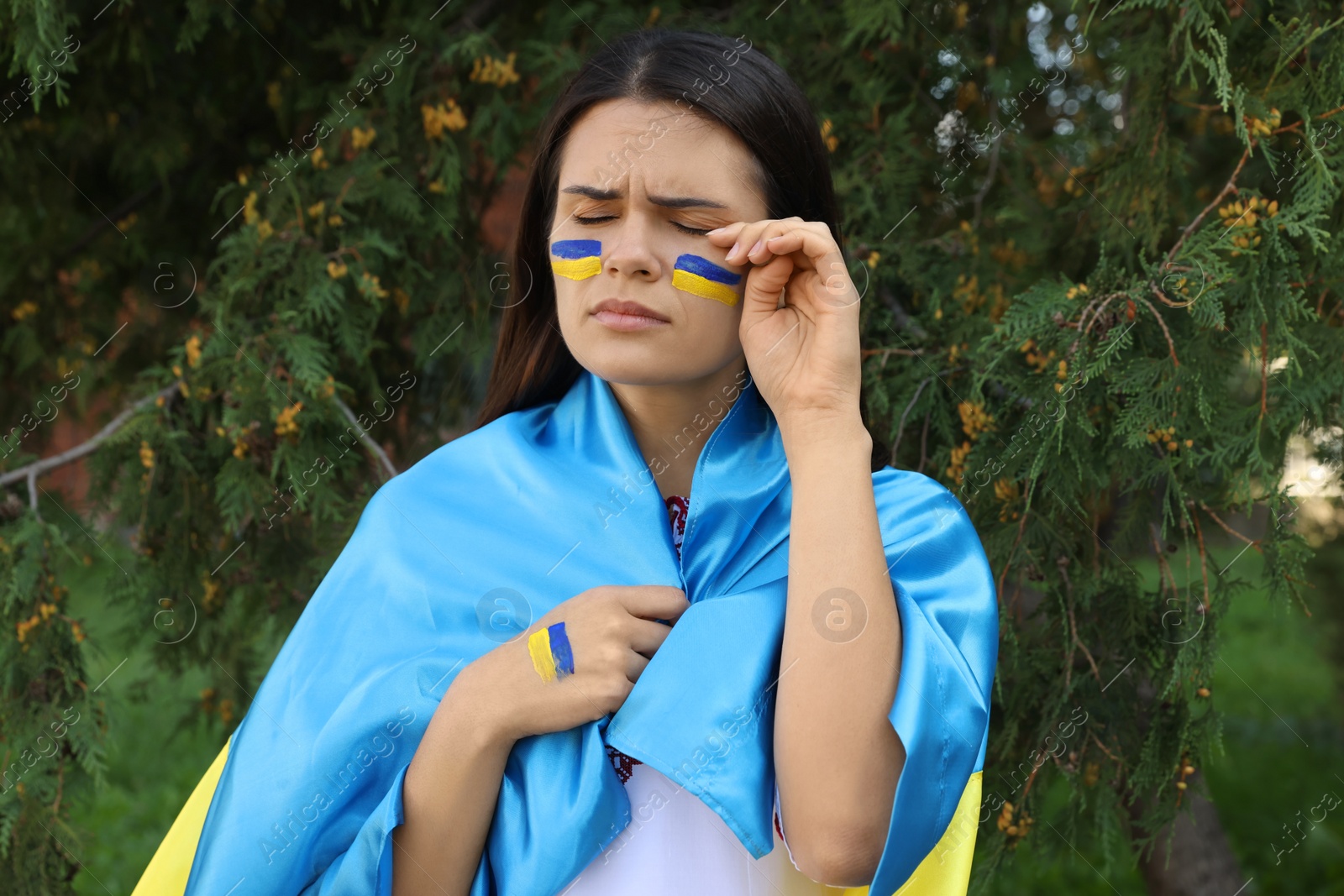 Photo of Sad young woman with Ukrainian flag outdoors