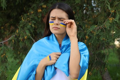 Sad young woman with Ukrainian flag outdoors
