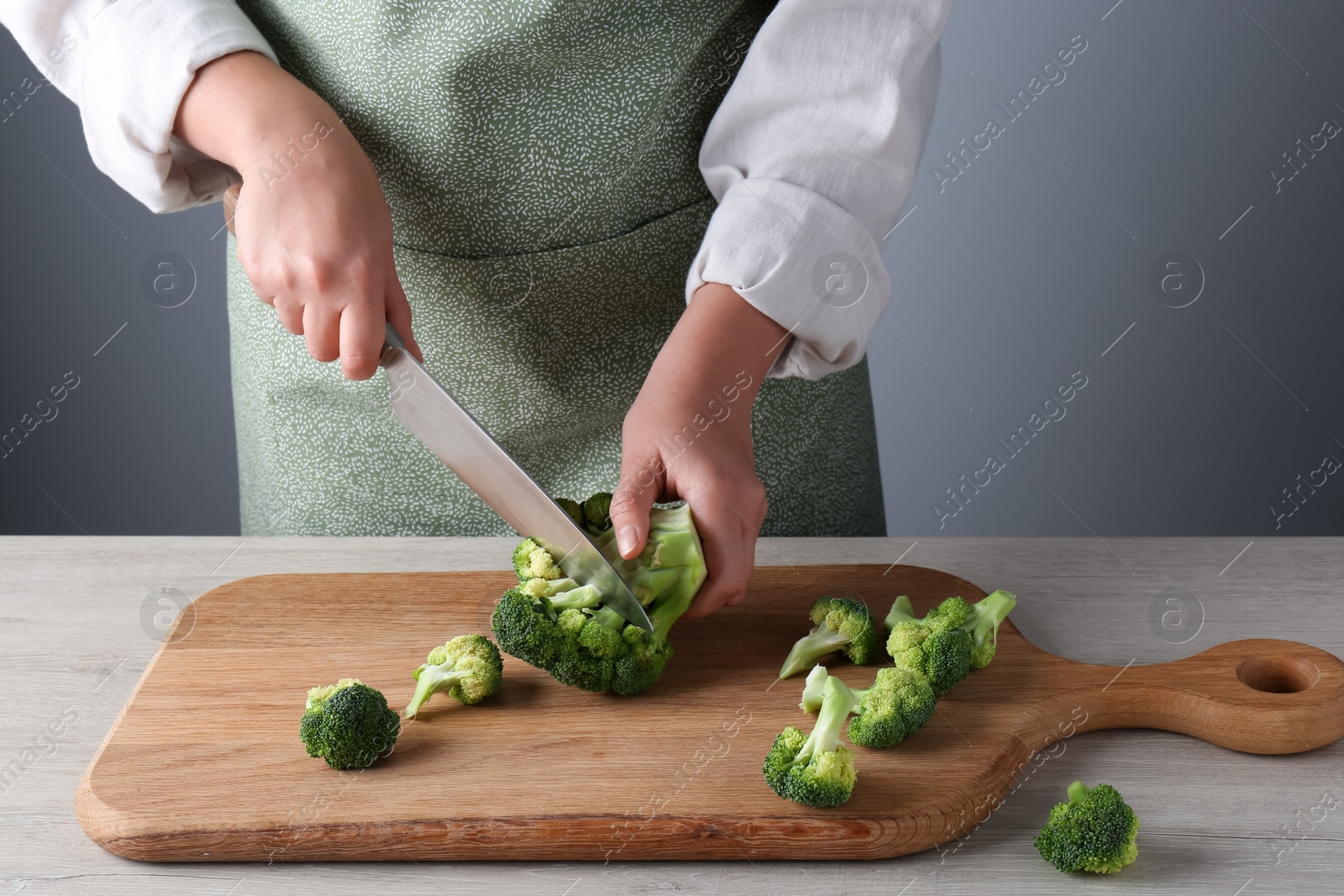 Photo of Woman cutting fresh broccoli at wooden table, closeup