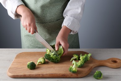 Photo of Woman cutting fresh broccoli at wooden table, closeup