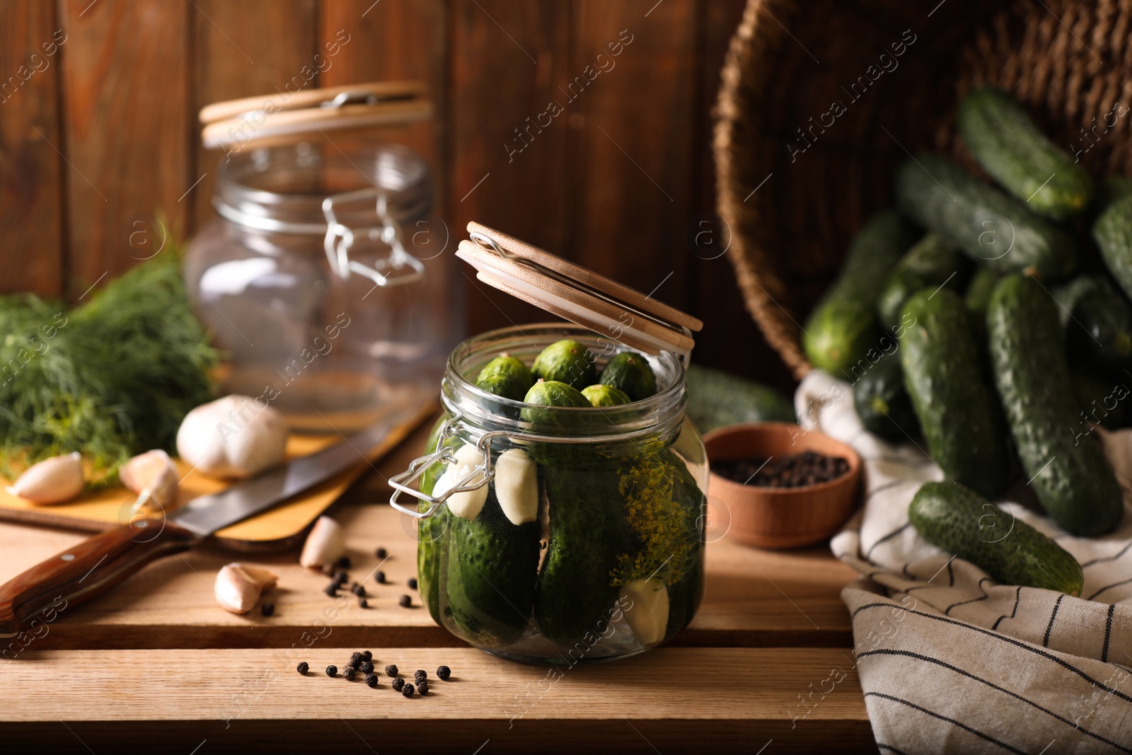 Photo of Glass jar with fresh cucumbers and other ingredients on wooden table. Canning vegetable